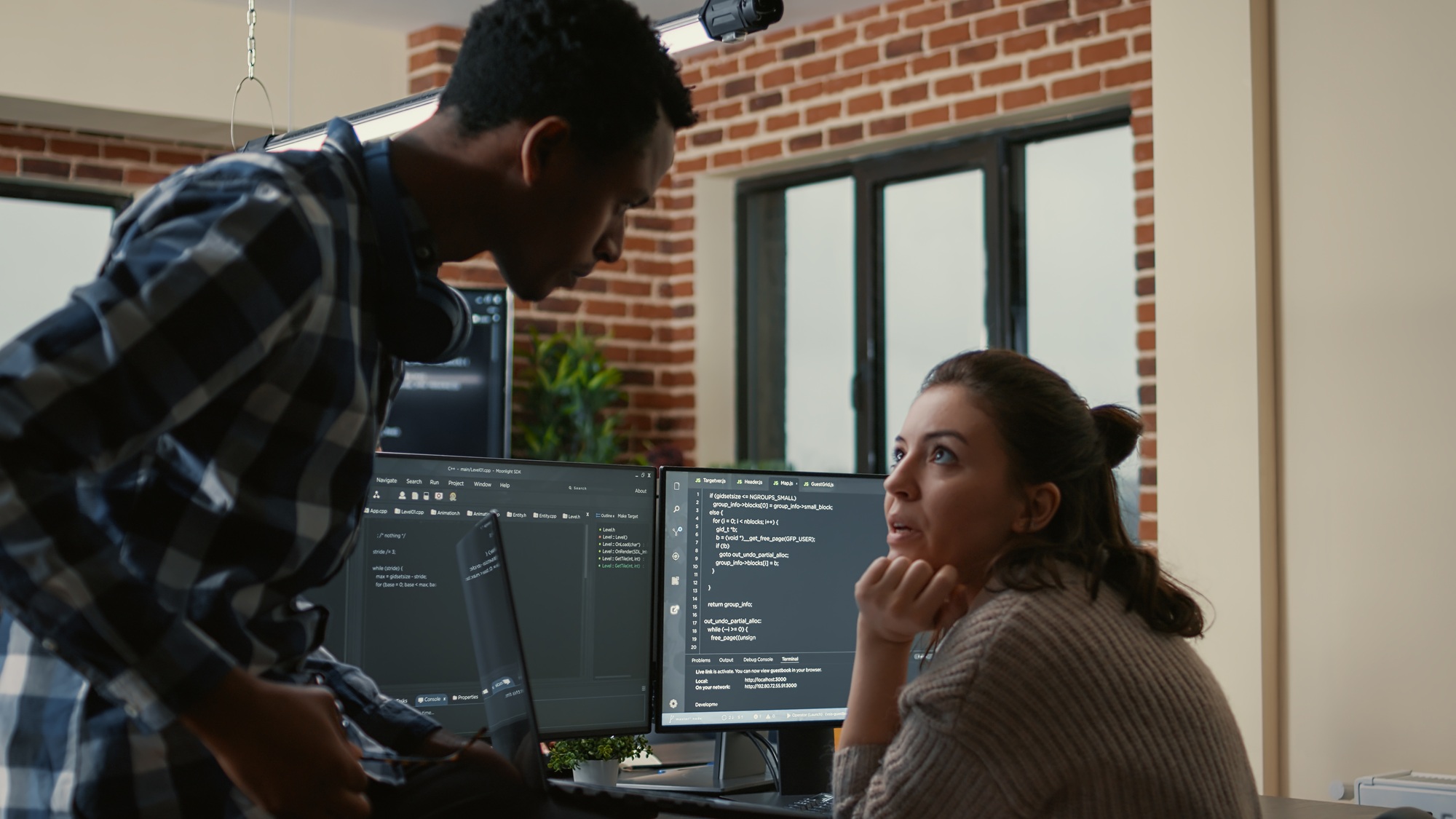 Junior developer sitting down on desk showing laptop with source code to senior dev
